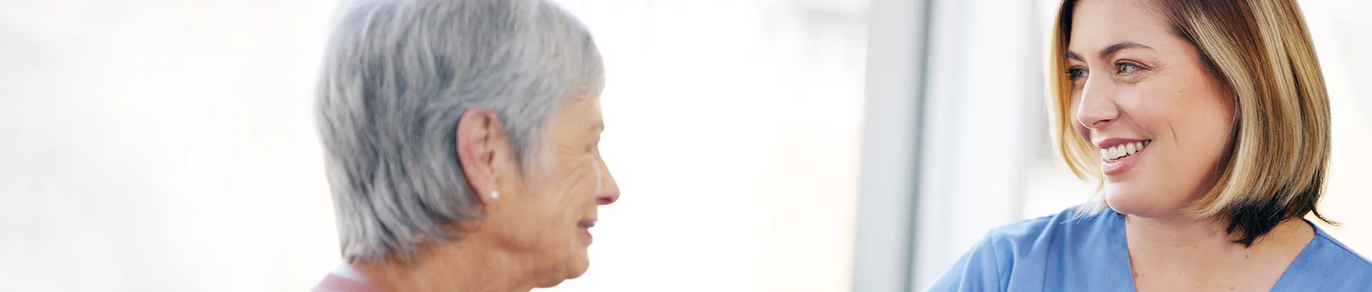 A close up of a young, female doctor smiling towards an older woman who is her patient.